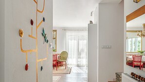 Een ruime woonkamer met een houten vloer, een groot tapijt, een kroonluchter en een eethoek op de achtergrond.