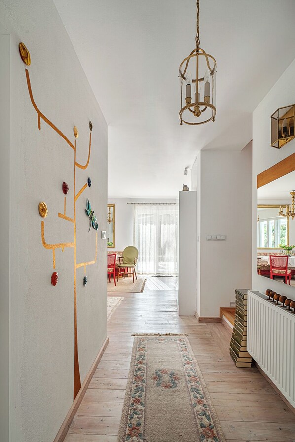 A spacious living area with a wooden floor, a patterned rug, a chandelier, and a wall with abstract art.