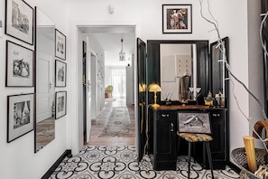 A hallway with framed photographs on the walls, a desk with a lamp, and a chair.
