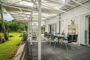A covered patio with a table and chairs, a garden view, and a bookshelf.