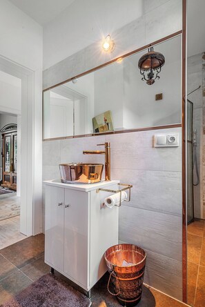 A bathroom with a white vanity, a copper bucket, a mirror, and a light fixture.