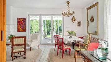 Zona pranzo con tavolo, sedie, un lampadario e vista attraverso porte in vetro.