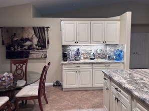 A kitchen with white cabinets, a granite countertop, a dining table with chairs, and a painting on the wall. - Perfect 3-bedroom house with a pool in enjoyable neighborhood (Indio)