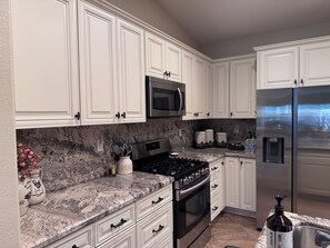 A kitchen with white cabinets, a stainless steel refrigerator, a microwave, a stove, and a water dispenser. - Perfect 3-bedroom house with a pool in enjoyable neighborhood (Indio)