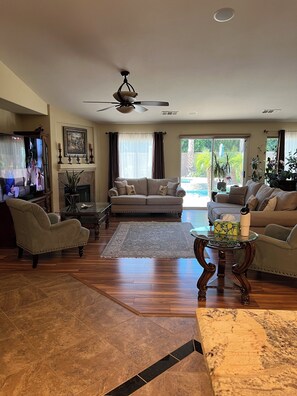 A living room with a sofa, armchairs, a glass coffee table, a fireplace, and a view of a pool. - Perfect 3-bedroom house with a pool in enjoyable neighborhood (Indio)