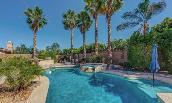 A swimming pool with palm trees, a hot tub, and a covered seating area. - Perfect 3-bedroom house with a pool in enjoyable neighborhood (Indio)