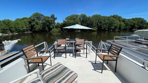 A boat deck with seating and tables, a canopy, and a view of a calm lake with trees. - 2-bedroom house boat in beautiful La Crosse with AC comfort (La Crosse)