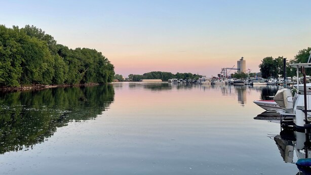 A calm river with boats docked on the right, a clear sky, and dense trees on the left. - 2-bedroom house boat in beautiful La Crosse with AC comfort (La Crosse)