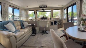 A cozy living area with a leather sofa, a round dining table, and a kitchen area with a control panel. - 2-bedroom house boat in beautiful La Crosse with AC comfort (La Crosse)
