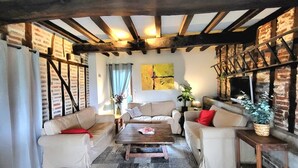 Un salon chaleureux avec des poutres apparentes, un mur en briques, un téléviseur et une cheminée.