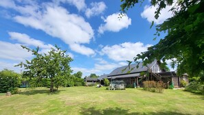 Un grand jardin avec une vaste pelouse, une maison en bois et un espace extérieur couvert.