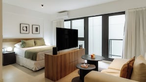 Una habitación de hotel moderna con cama, televisión, sofá y un ventanal grande.