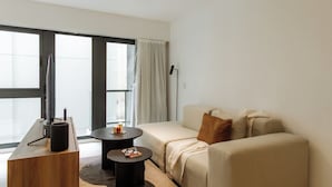 Una sala de estar moderna con un sofá, una mesa de centro, un televisor y un amplio ventanal con cortinas.