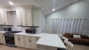 Una cocina compacta con armarios blancos, un microondas, una estufa a gas y un comedor con mesa y sillas blancas.
