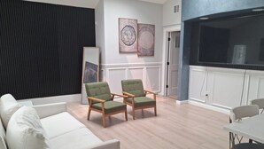 Una sala moderna con un sofá blanco, dos sillones verdes, un televisor de pantalla plana y una mesa de comedor.