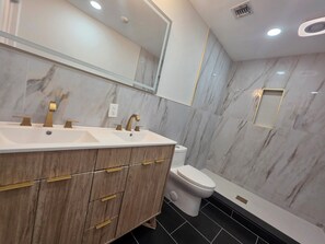 Un baño moderno con tocador de mármol, inodoro y zona de ducha.