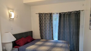 Quarto com cama, luminária de cabeceira, mesa de cabeceira e janela com cortinas estampadas.