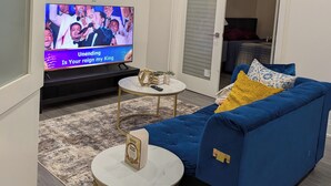 Uma sala de estar moderna com televisão de tela plana, um sofá azul, duas mesinhas redondas e um tapete estampado.