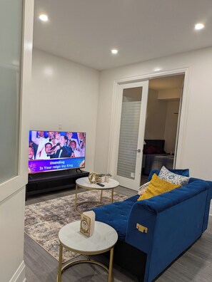 A modern living room with a flat-screen TV, a blue sofa, two small round tables, and a patterned rug. - Perfect 3-bedroom apartment with AC in vibrant Toronto (Toronto)