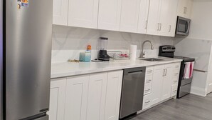 A modern kitchen with white cabinets, stainless steel appliances, and a grey floor. - Perfect 3-bedroom apartment with AC in vibrant Toronto (Toronto)
