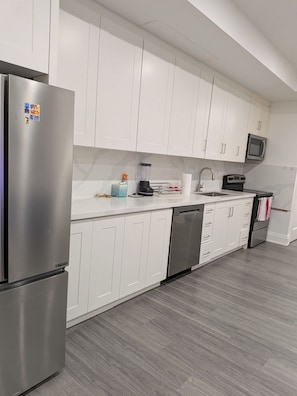 A modern kitchen with white cabinets, stainless steel appliances, and a grey floor. - Perfect 3-bedroom apartment with AC in vibrant Toronto (Toronto)