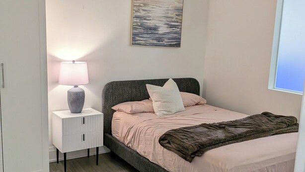 Um quarto com cama, abajur, um quadro na parede e um guarda-roupa.