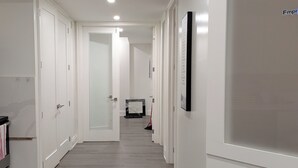 Um corredor com paredes brancas, piso cinzento e uma porta no final que dá para outro cômodo.