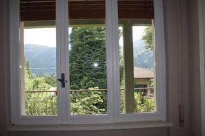 A window with a view of a mountainous landscape and a house with a green roof.