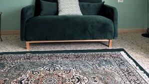 A room with a dark green couch, a patterned rug, and four framed pictures on the wall.