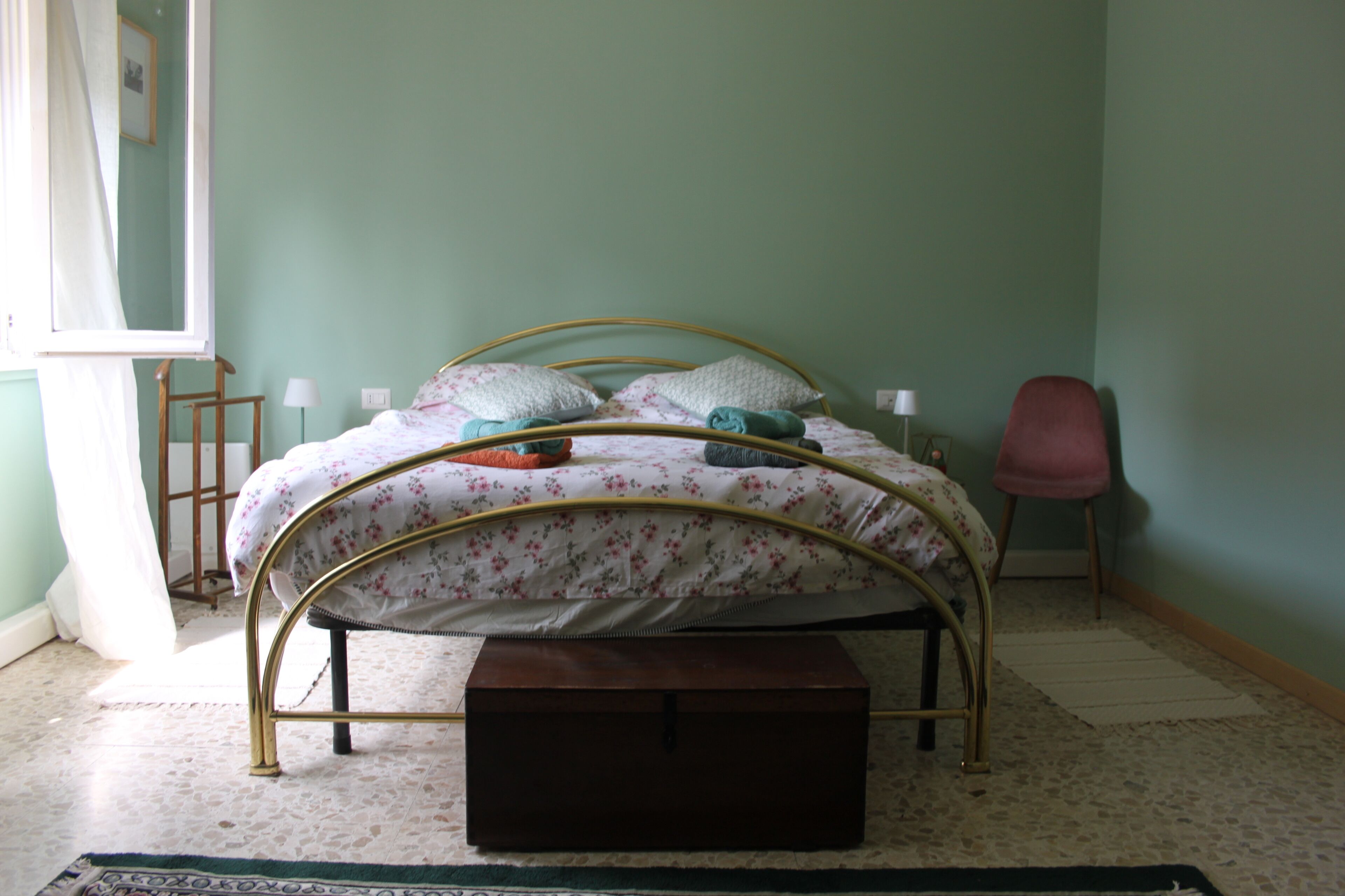 Ein Bett mit floralem Überwurf, eine hölzerne Bank, ein Stuhl und ein kleiner Tisch.