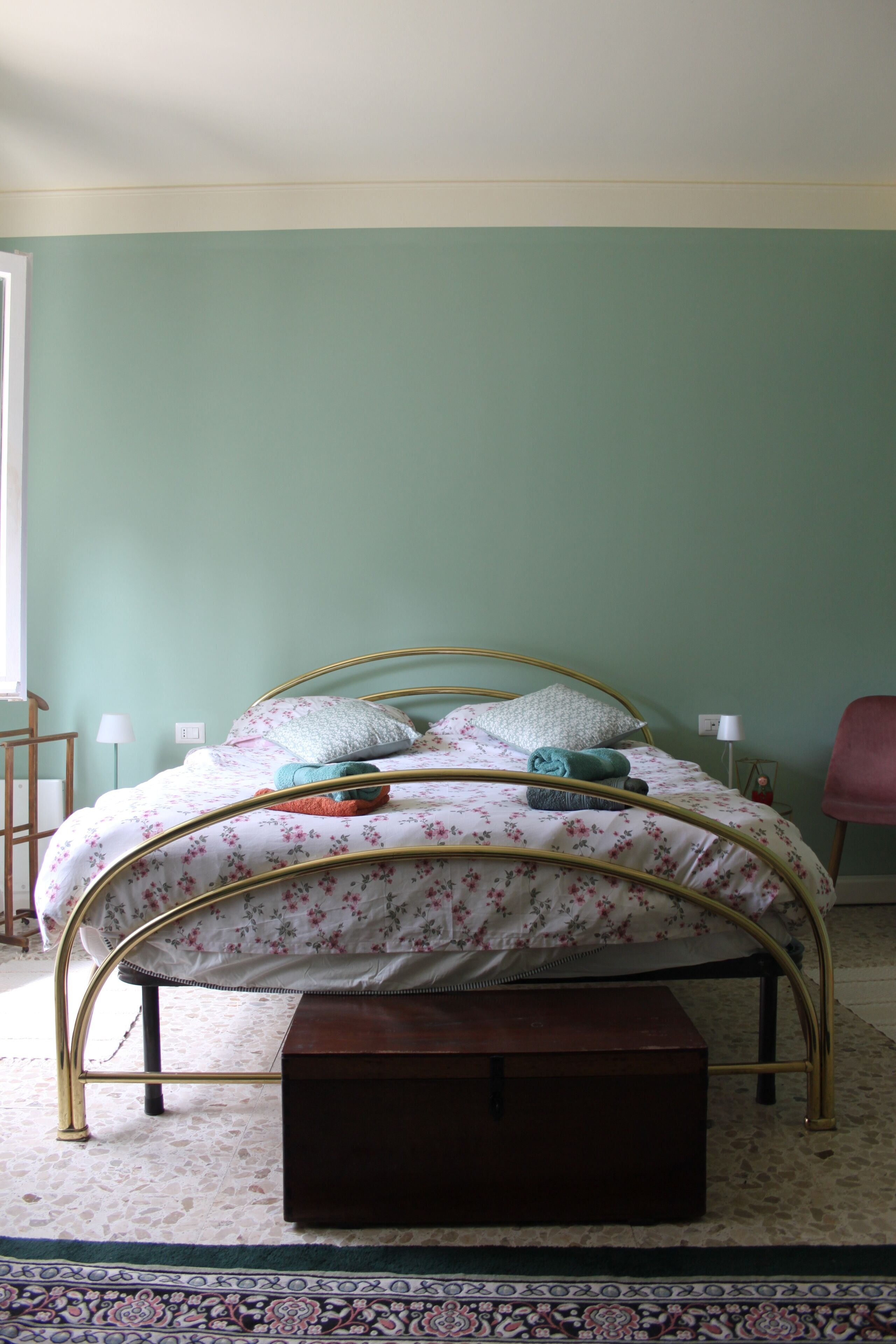 Una cama con colcha estampada, una mesita de noche, una lámpara y una silla en una habitación con paredes verdes.