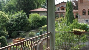 A covered outdoor area with a tiled floor, a metal railing, and a view of a brick building with a tower.