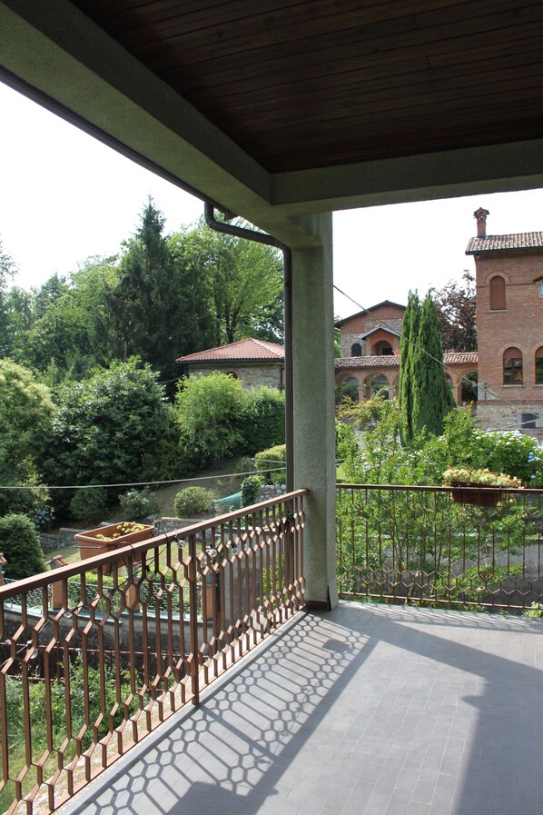A covered outdoor area with a tiled floor, a metal railing, and a view of a brick building with a tower.