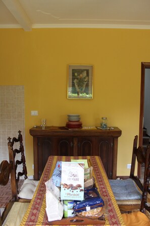 Una sala da pranzo con un tavolo di legno, sedie, una parete gialla e un quadro incorniciato.