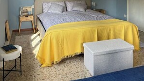 A bedroom with a bed, bedside tables, a chair, a bench, and a door.