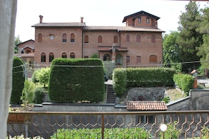 Un ampio edificio in mattoni con numerose finestre e un tetto in tegole, circondato da siepi curate e un muro in pietra.