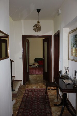 A hallway with a patterned rug, a wooden table with a chair, and a hanging light fixture.