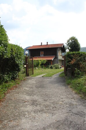 A house with a red roof, a gravel path leading to a gated entrance, and a number 27 sign on the gate.