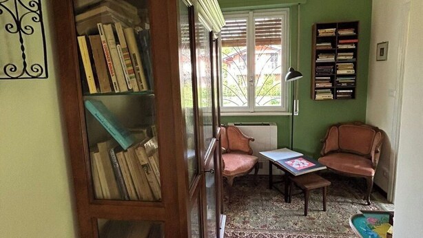 A room with a bookshelf, two chairs, a table, and a window with blinds.