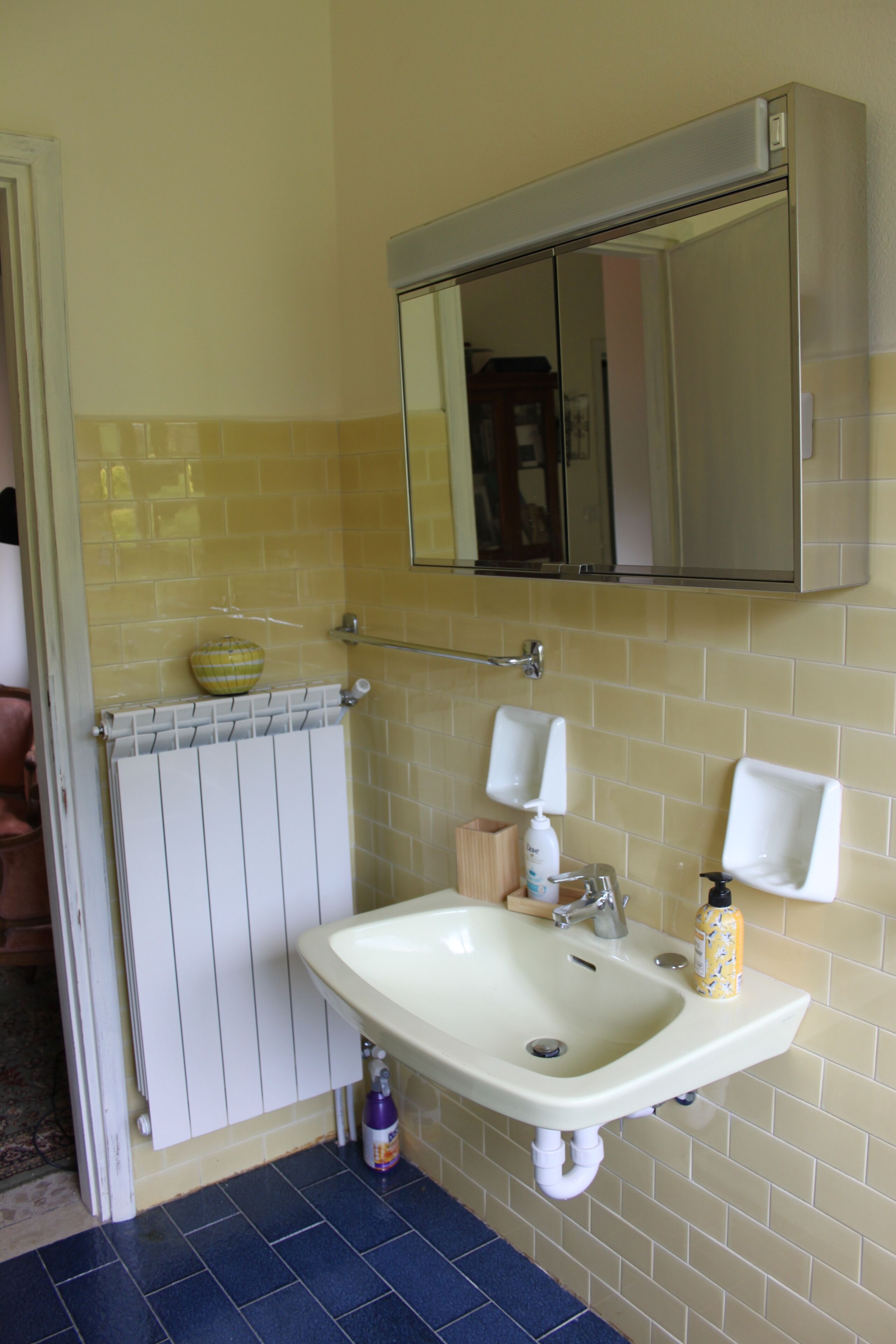 A bathroom with a white sink, a mirror above it, and a yellow-tiled wall.