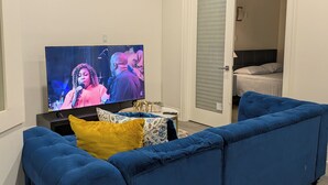 Un salon avec un canapé bleu, un téléviseur diffusant une émission et une petite table sur laquelle est posé un objet décoratif.