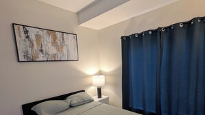 Une chambre à coucher avec un lit, une lampe de chevet, une œuvre d’art accrochée au mur et une fenêtre avec des rideaux.