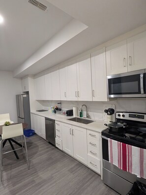 A modern kitchen with white cabinets, a stainless steel microwave, a stove, and a sink. - Adorable 3-bedroom unit with AC in vibrant Toronto (Toronto)