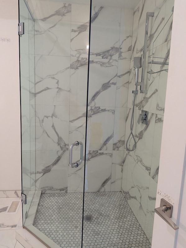 A glass-enclosed shower with a marble wall, a handheld showerhead, and a floor with hexagonal tiles. - Adorable 3-bedroom unit with AC in vibrant Toronto (Toronto)