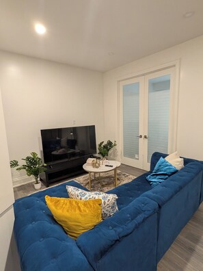 Un saló amb un sofà blau, una televisió i una taula rodona petita amb objectes decoratius.