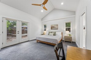 Quarto com cama, ventilador de teto, mesa de cabeceira, luminária e vista para o exterior por uma porta de correr.
