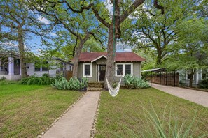 Uma casa com jardim frontal, uma rede e um caminho que leva à casa.