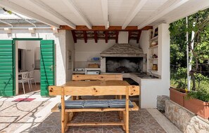 Eine rustikale Außenküche mit Steinofen, Holzmöbeln und einer grünen Tür.