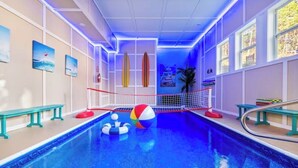 Une piscine intérieure équipée d’un filet de volley-ball, de bancs et de planches de surf accrochées au mur.