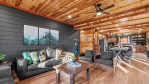 Un salon spacieux avec un canapé gris foncé, un plafond en bois et un coin repas comprenant une table et des chaises.